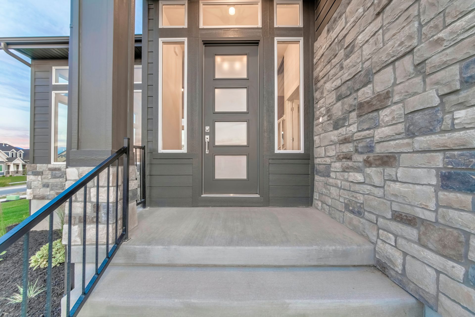 Gray front door with sidelights, stone wall, concrete steps, and black railing. Gray front door with sidelights, stone wall, concrete steps, and black railing.