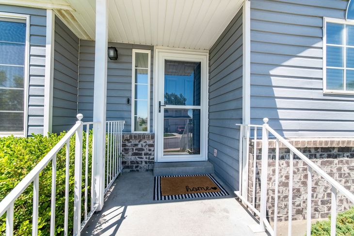 Gray house front door with white railings, a welcome mat, and sidelight window.