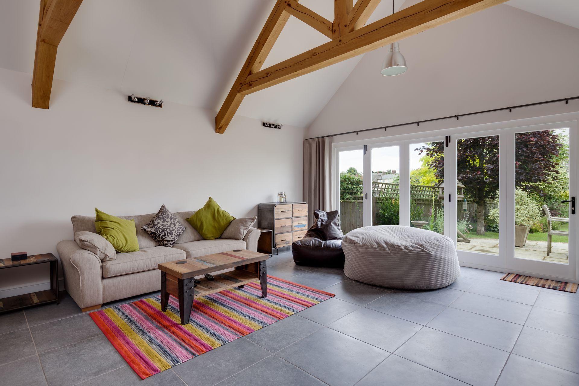 Living room with cream sofa, colorful rug, sliding doors, and exposed wooden beams. Living room with cream sofa, colorful rug, sliding doors, and exposed wooden beams.