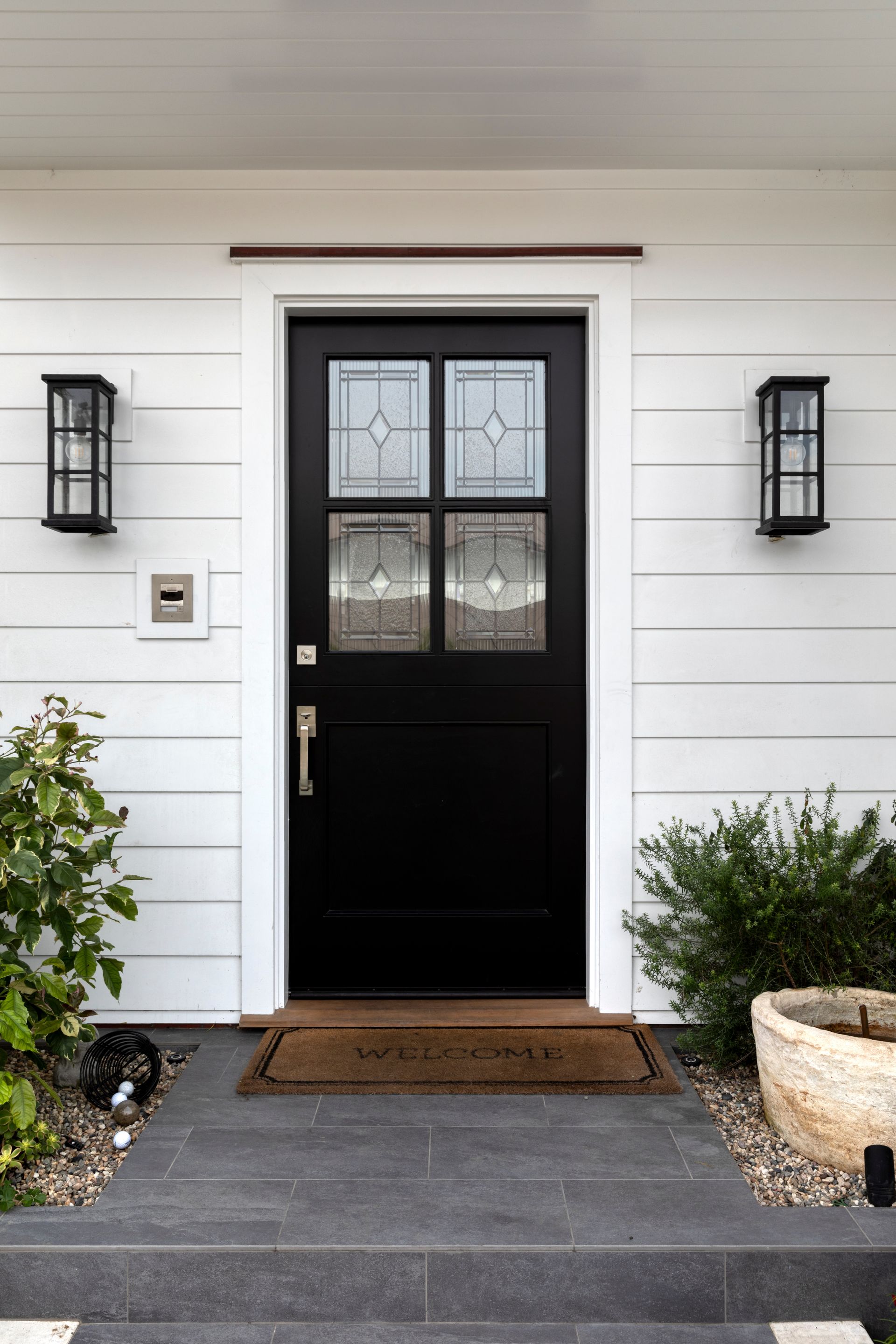 Black front door with glass panels, flanked by sconces, on a white house.