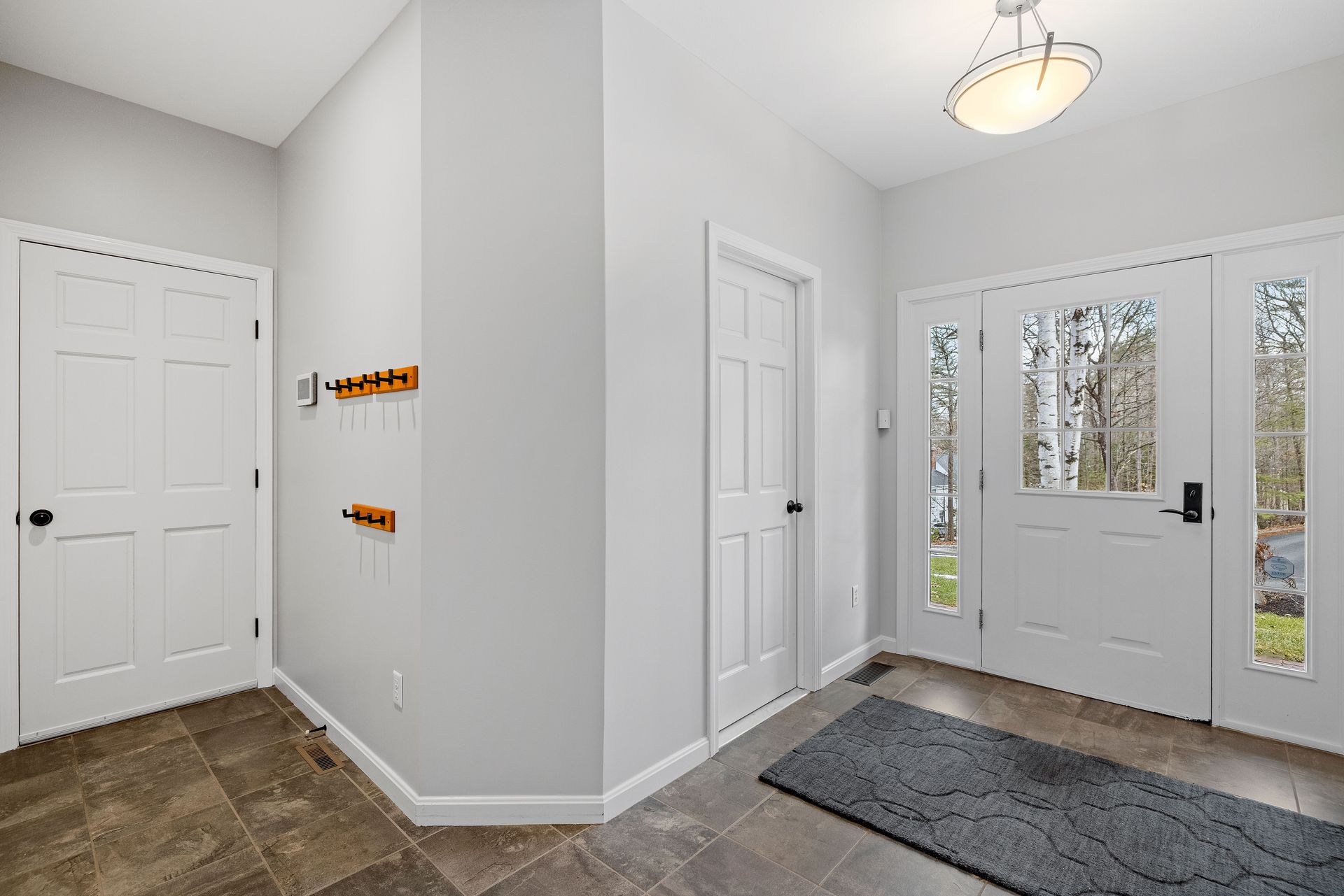 Bright entryway with white interior doors, tiled flooring, and a glass-paneled front door. Bright entryway with white interior doors, tiled flooring, and a glass-paneled front door.