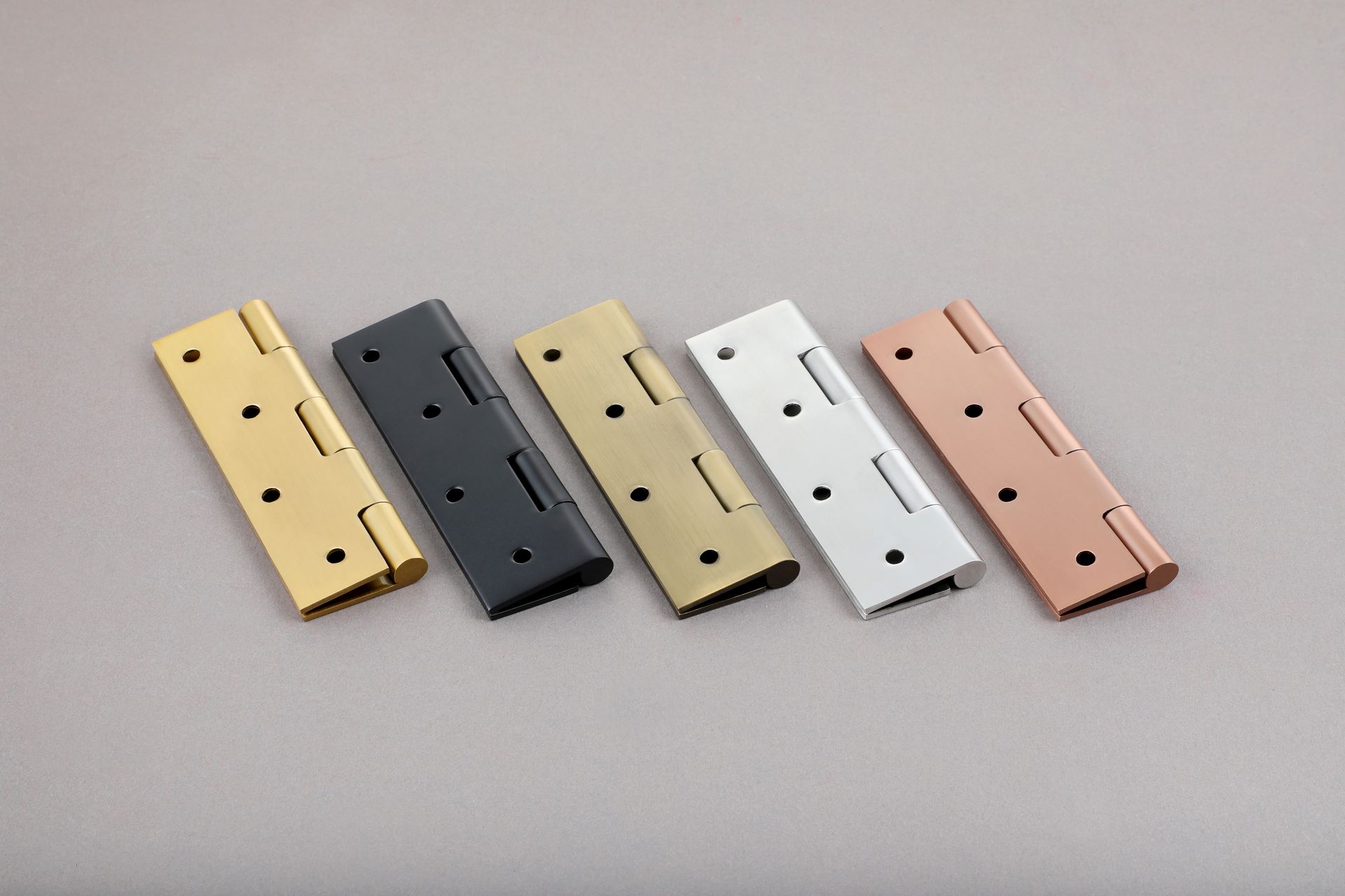 Five metal hinges in gold, black, tan, white, and copper, lying on a gray surface. Five metal hinges in gold, black, tan, white, and copper, lying on a gray surface.