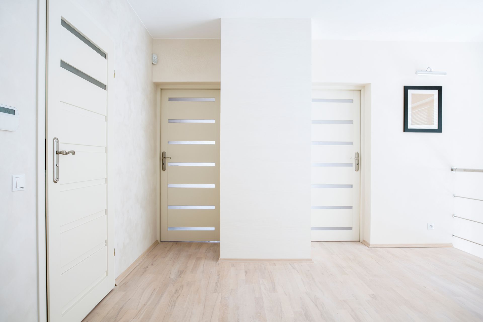 Three white doors in a hallway with wood flooring and a framed picture on the wall. Three white doors in a hallway with wood flooring and a framed picture on the wall.