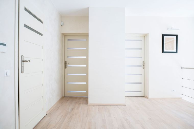 Three white doors in a hallway with wood flooring and a framed picture on the wall.
