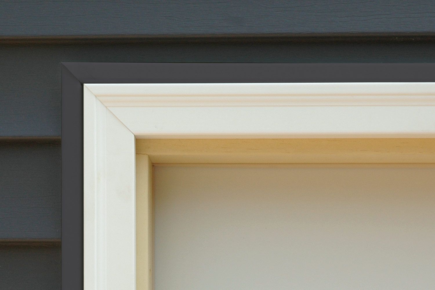 Corner of door frame with dark gray trim around a white frame, against gray siding.