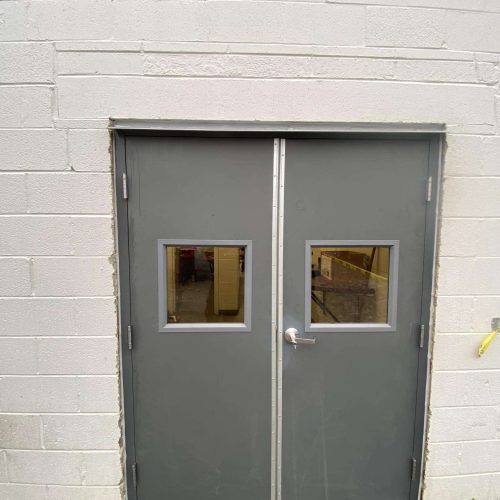 Gray double doors with small square windows in a white cinder block wall. Gray double doors with small square windows in a white cinder block wall.