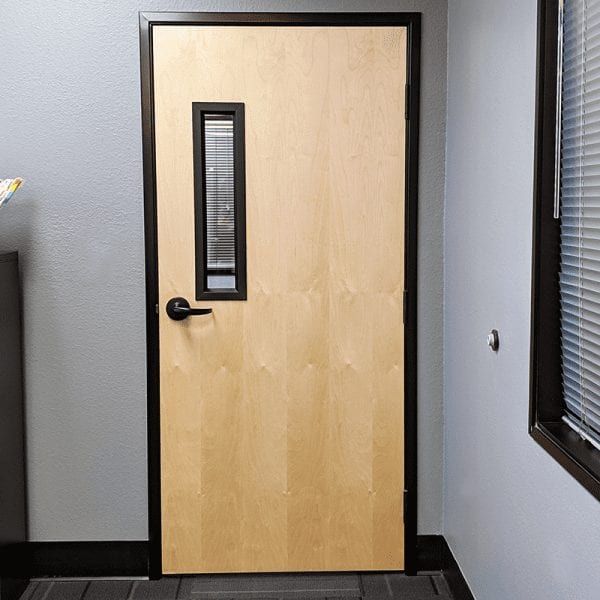 Wooden door with small rectangular window and black frame, set in a light grey wall. Wooden door with small rectangular window and black frame, set in a light grey wall.
