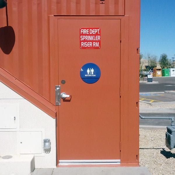 Orange door with signs for a fire dept riser room and restroom, on an orange building exterior. Orange door with signs for a fire dept riser room and restroom, on an orange building exterior.