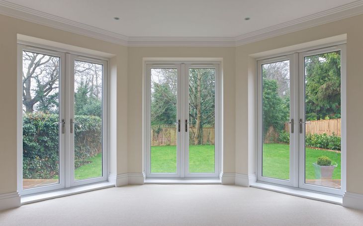Bright, neutral room with three white-framed glass doors looking onto a green yard with trees and bushes.