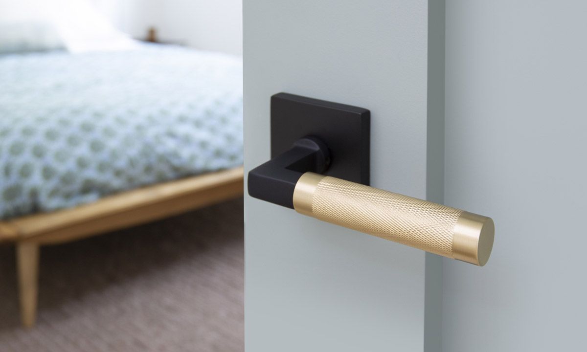 Black and gold door handle on a light blue door in a bedroom, bed in the background. Black and gold door handle on a light blue door in a bedroom, bed in the background.