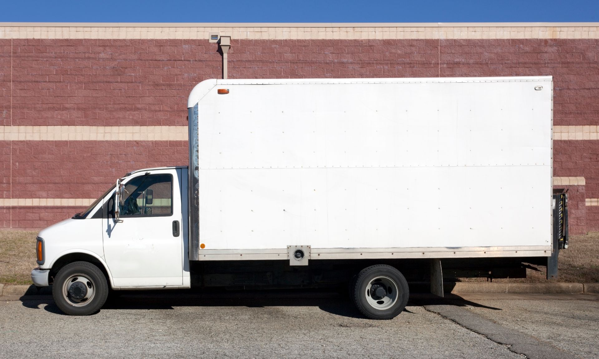White delivery truck speeding on a highway with blurred green trees in background.