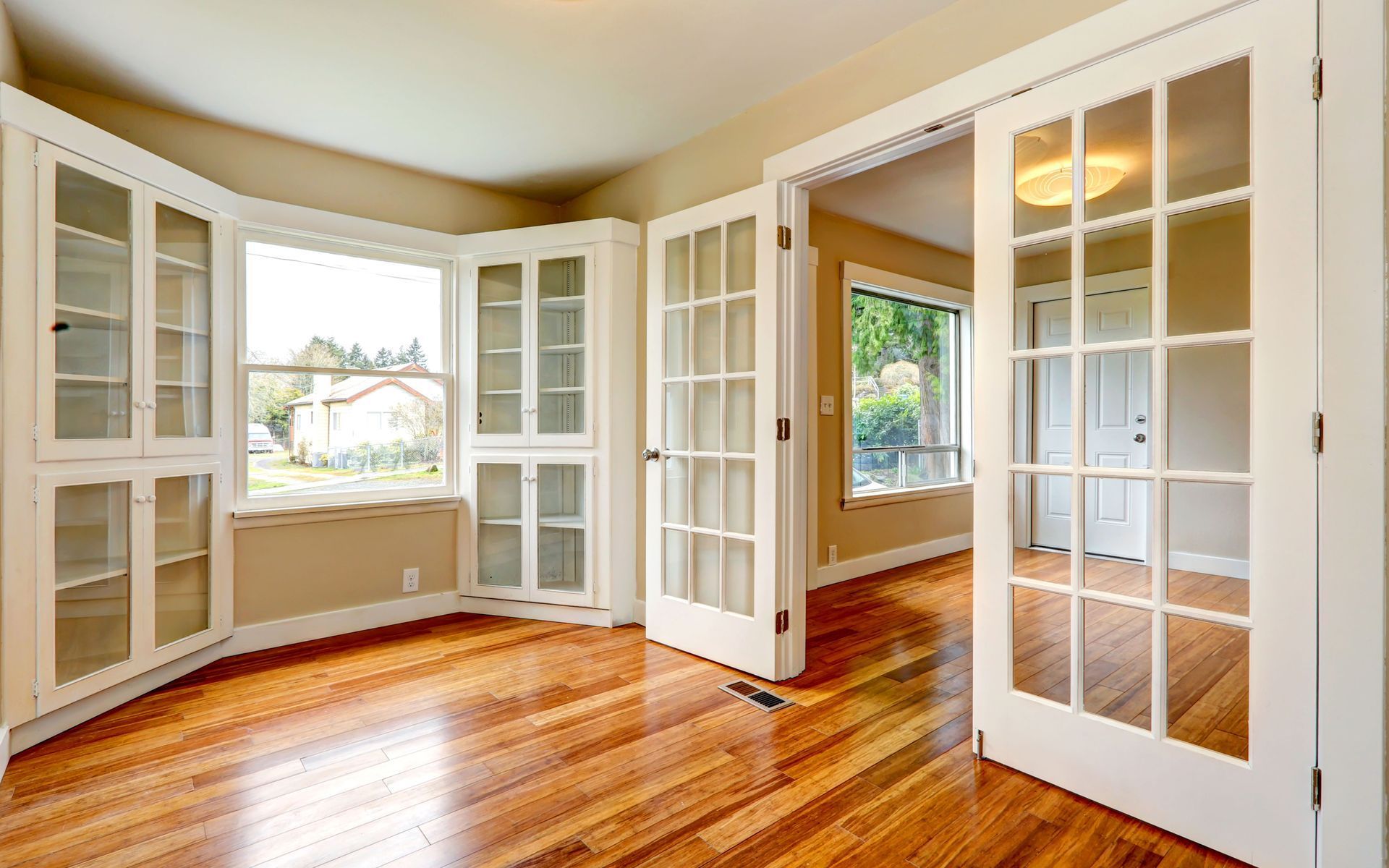 Empty room with hardwood floors, built-in white cabinets, and French doors. Empty room with hardwood floors, built-in white cabinets, and French doors.