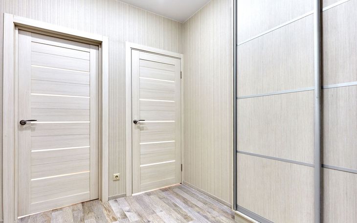 Light-colored room with two doors and a sliding closet. Light wood-look walls and floor.