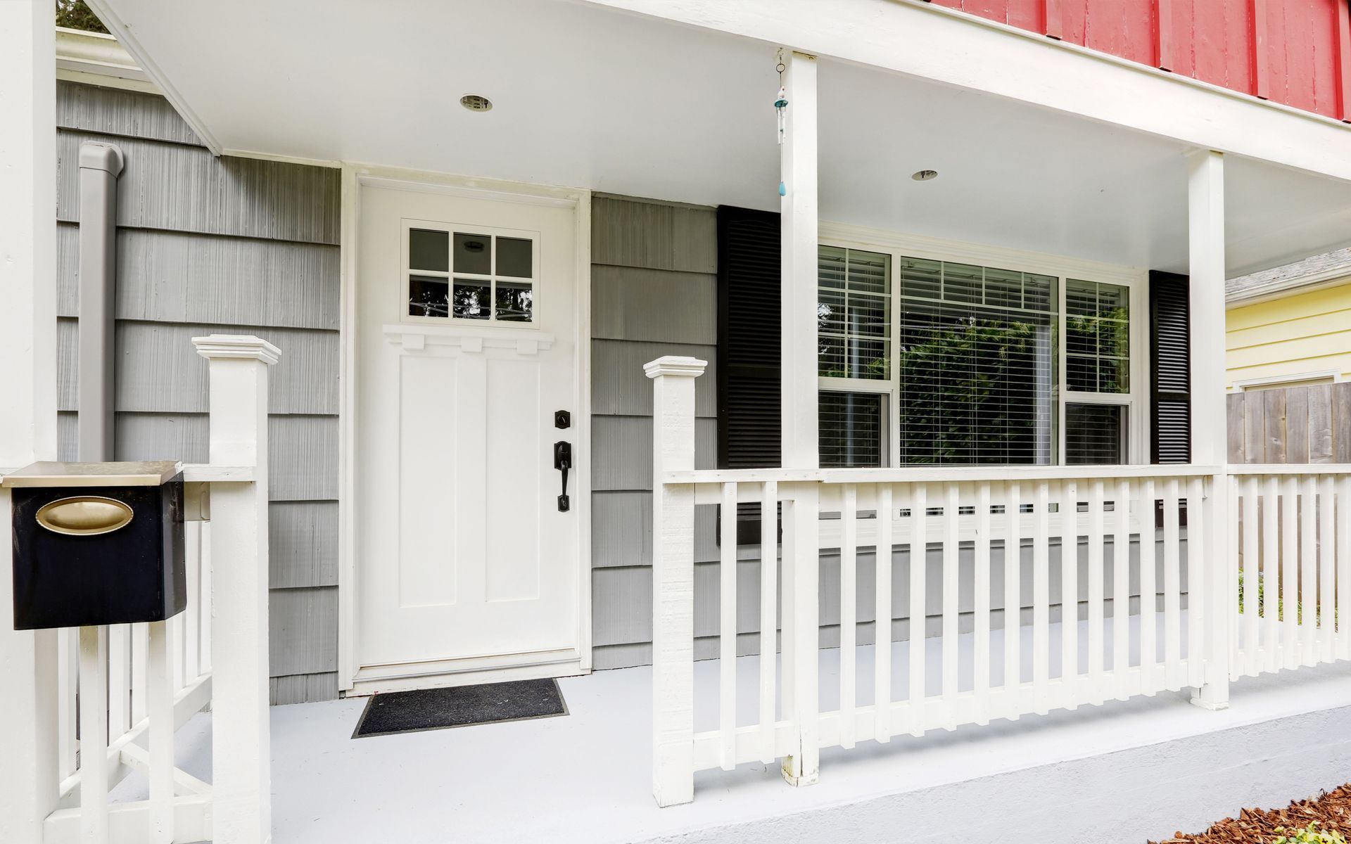 White front porch with a door, mailbox, and windows; gray siding. White front porch with a door, mailbox, and windows; gray siding.
