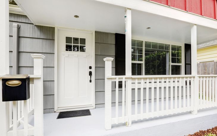 White front porch with a door, mailbox, and windows; gray siding.