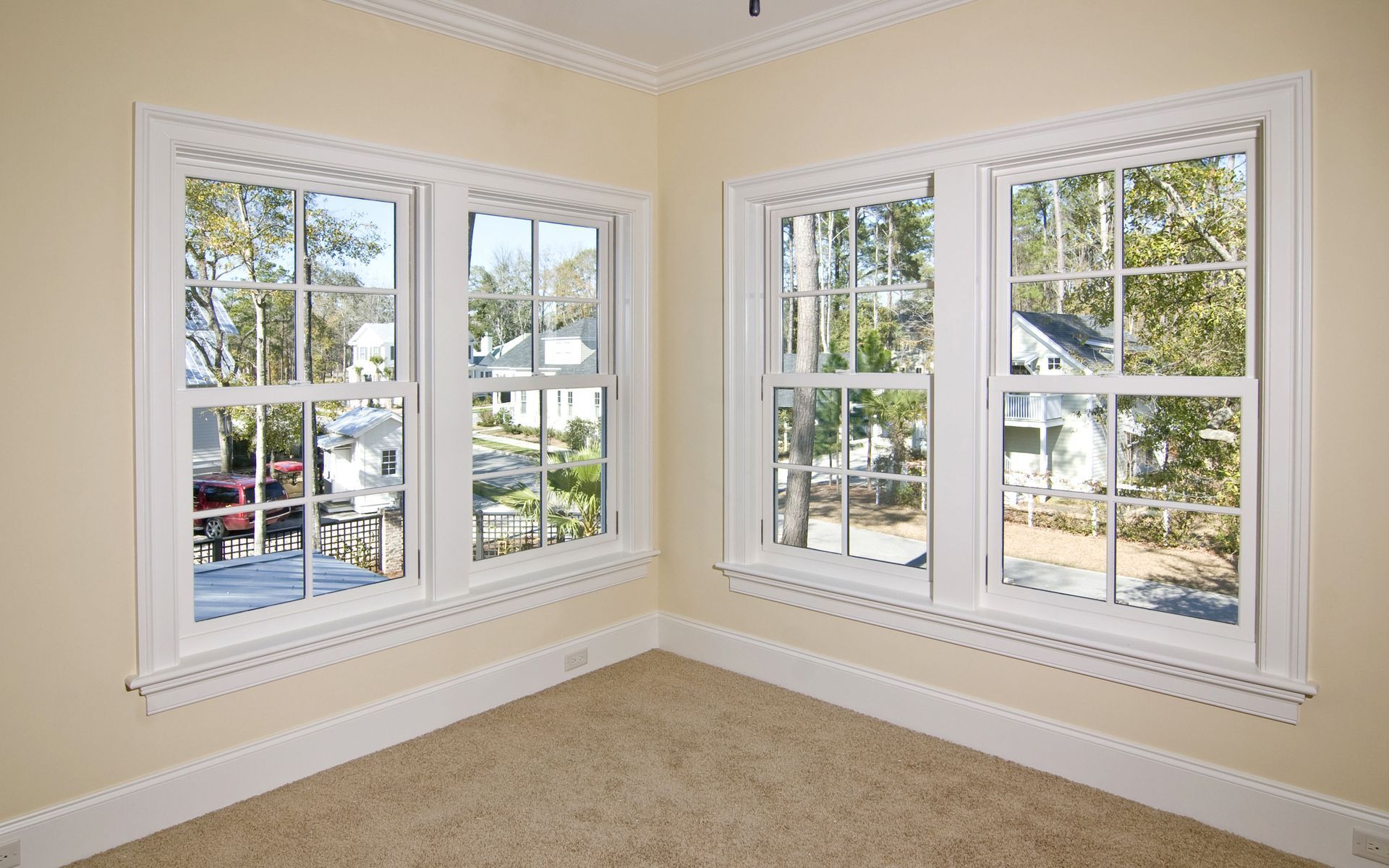 Corner of a room with two sets of white-framed windows, beige walls, and tan carpet. Corner of a room with two sets of white-framed windows, beige walls, and tan carpet.