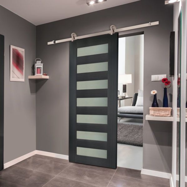 Gray sliding door with frosted glass panels, mounted on a track in a gray hallway.