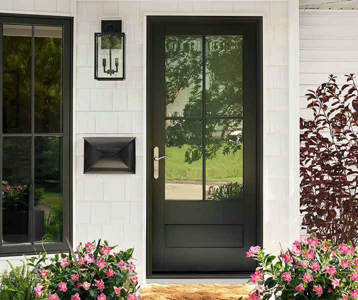 Black front door with glass panes, brass handle, surrounded by white siding and pink flowers. Black front door with glass panes, brass handle, surrounded by white siding and pink flowers.