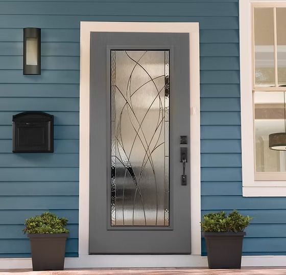 Gray front door with decorative glass, blue siding, mailbox, and potted plants.