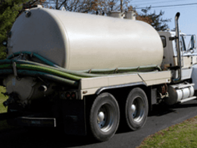 A beige vacuum truck with green hoses parked on asphalt.