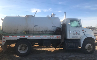 A white vacuum truck parked on a dirt lot, featuring a large cylindrical tank mounted on the bed.