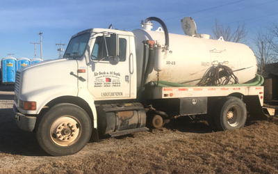 A white vacuum truck used for septic service parked on a gravel lot near several portable toilets.