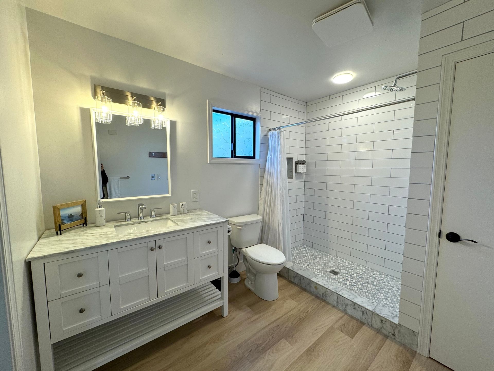A bathroom with a toilet , sink , mirror and walk in shower.