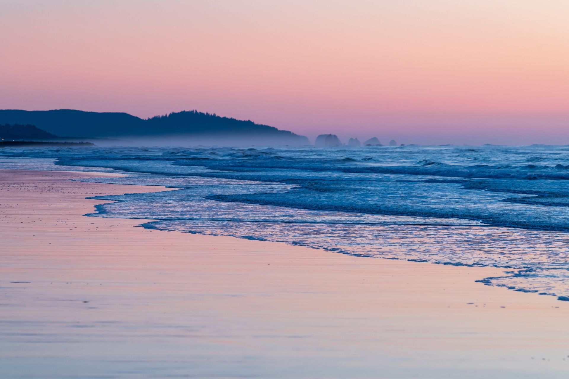 A beach with waves crashing on the shore at sunset.