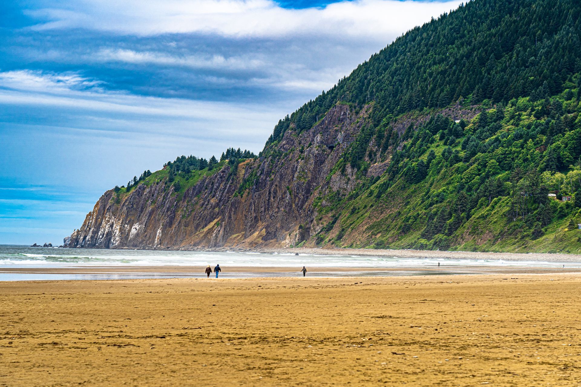 A beach with a mountain in the background and people walking on it.