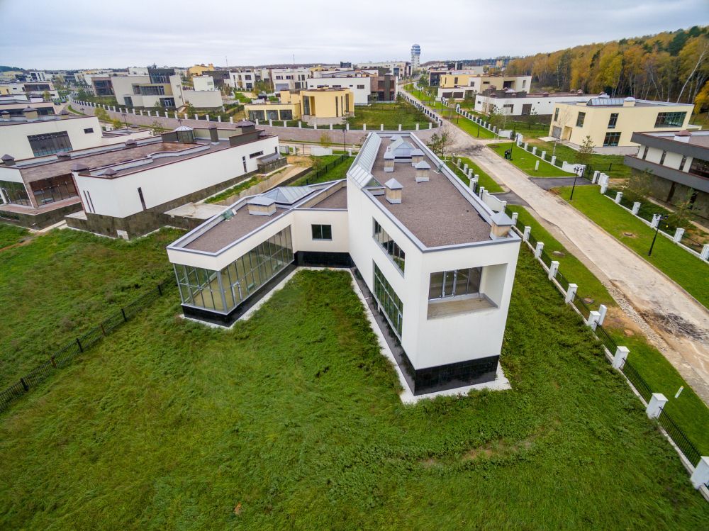 Aerial view of a modern white house with a gray roof in a grassy residential neighborhood