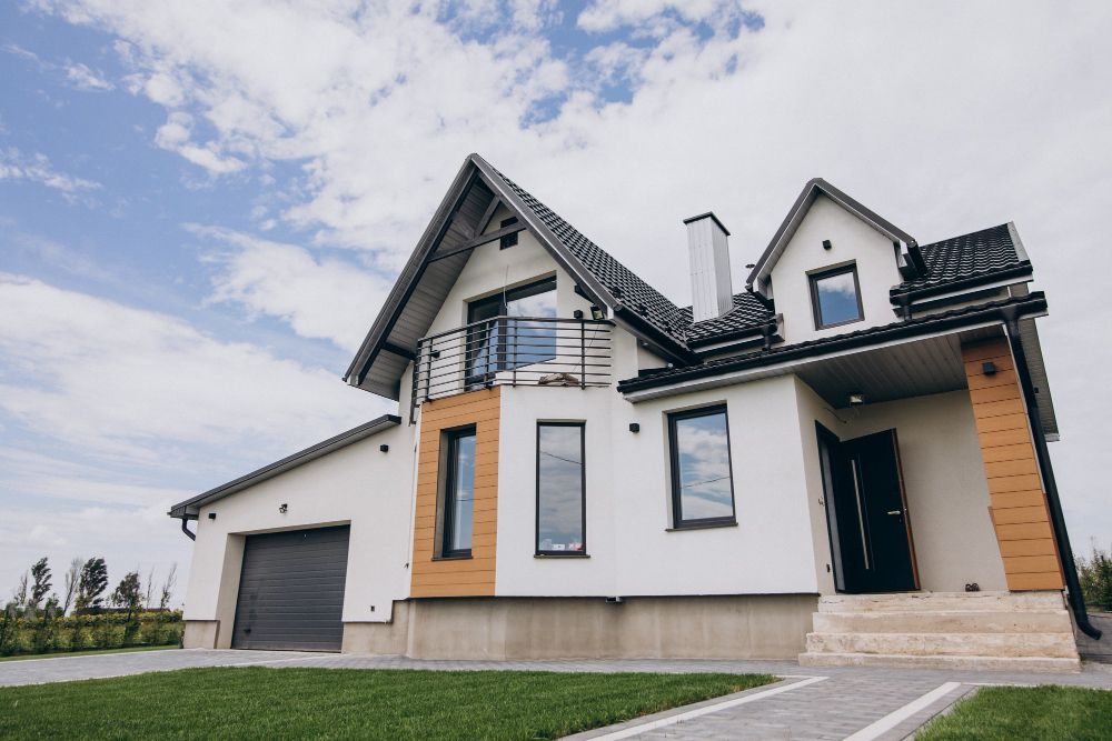 Modern two-story house with white walls, wood accents, dark roof, and a garage under a cloudy sky
