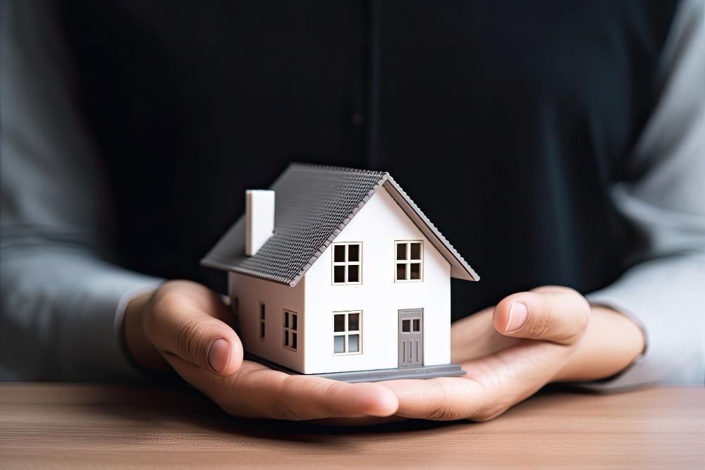 Hands holding a small model house on a wooden table, symbolizing home or property support