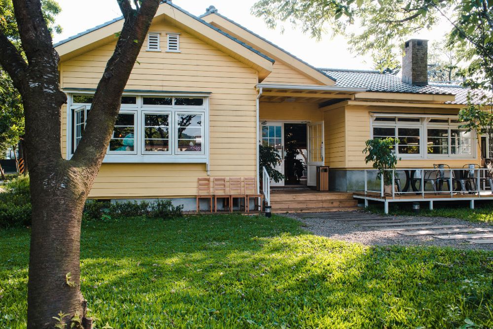 Yellow house with a front porch, white trim, and a green lawn shaded by trees
