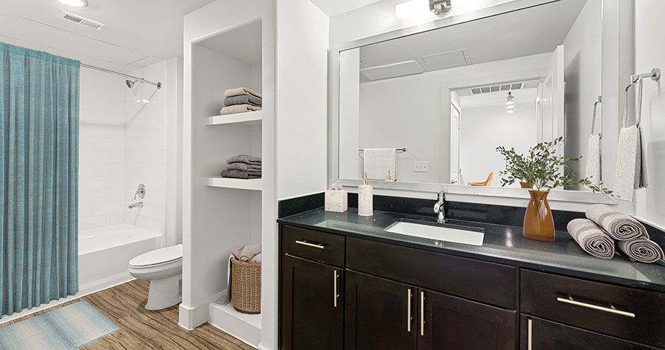 Bathroom with dark wood cabinets, large mirror, turquoise shower curtain, and built-in shelving at The Standard at Domain NORTHSIDE, offers luxury apartments in North Austin.