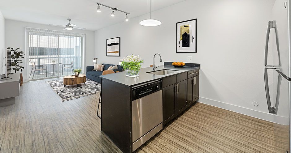 Modern apartment interior with kitchen island, living area with balcony access, and light wood floors at The Standard at Domain NORTHSIDE, offers furnished apartments in North Austin.