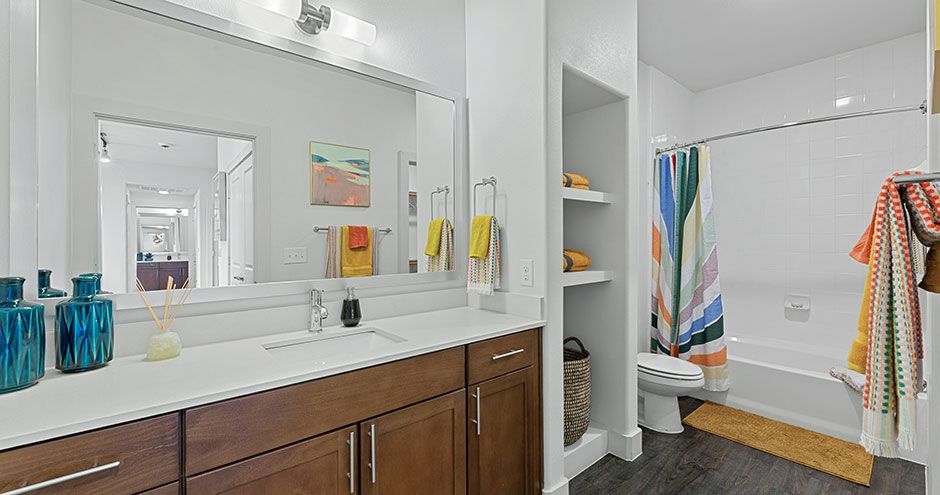 Bathroom with white countertop, dark wood cabinets, large mirror, shower with colorful curtain, and built-in shelves at The Standard at Domain NORTHSIDE, offers apartments near The Domain Austin.