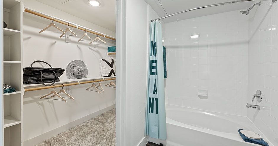Bathroom with white tile, tub, and shower curtain at The Standard at Domain NORTHSIDE, offers apartments at The Domain. Closet with clothes and shelves.