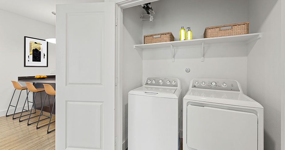 Laundry room with washer and dryer, shelves, baskets, and door to a kitchen at The Standard at Domain NORTHSIDE, offers luxury apartments in North Austin.
