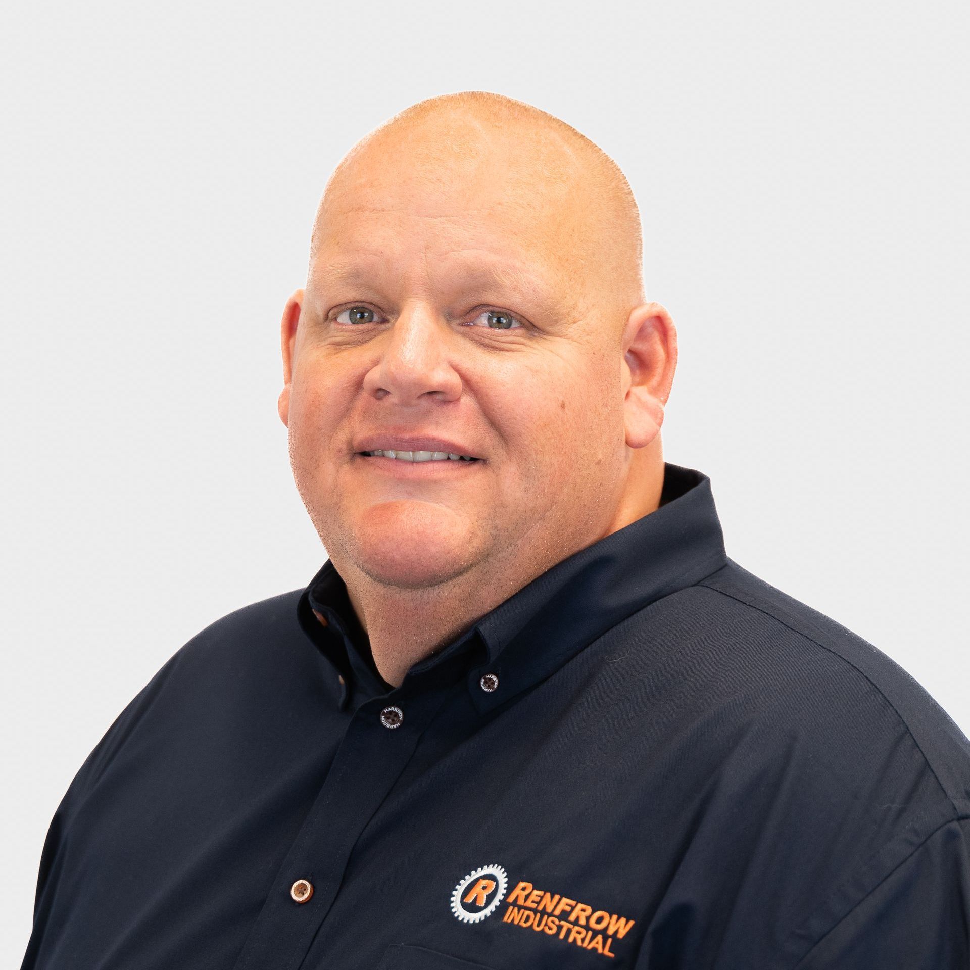Bald man in navy shirt with Renprow Industrial logo smiling, against white backdrop.