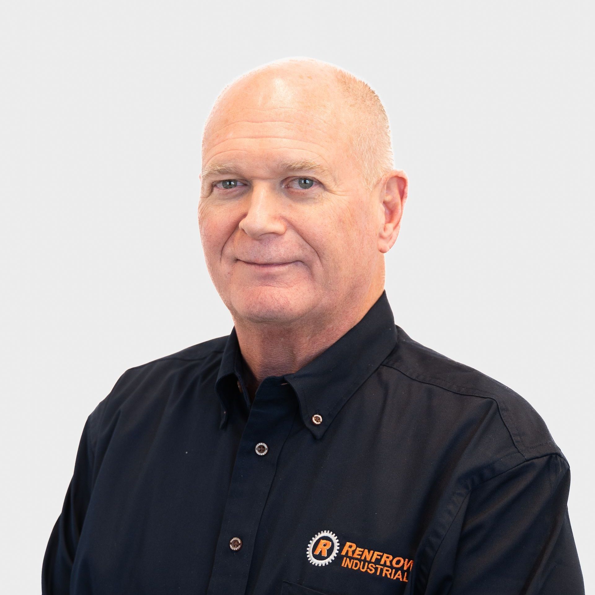 Bald man in a black button-down shirt, logo on chest, smiles at the camera, plain background.