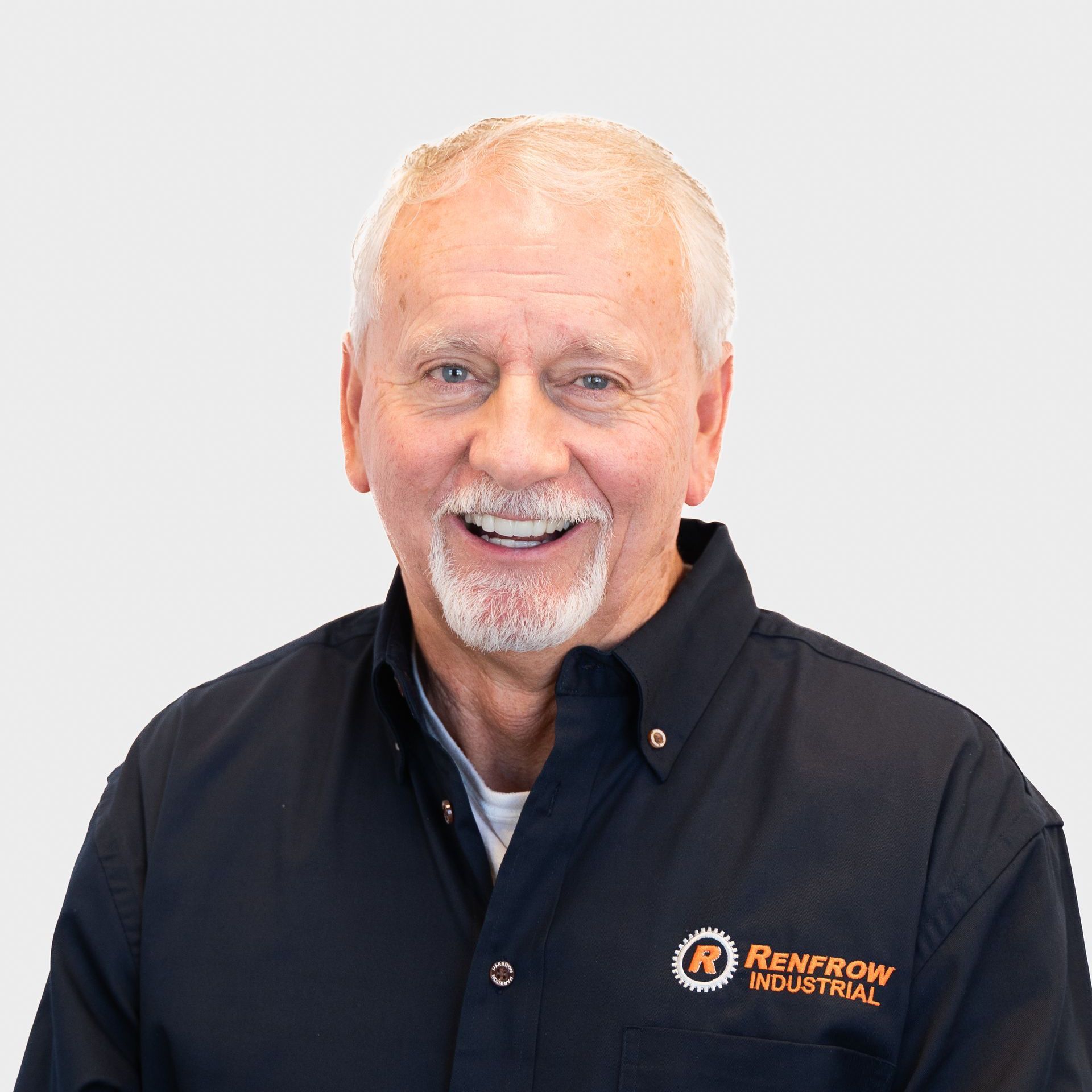 Smiling older man with gray hair and beard wearing a black shirt with a company logo.