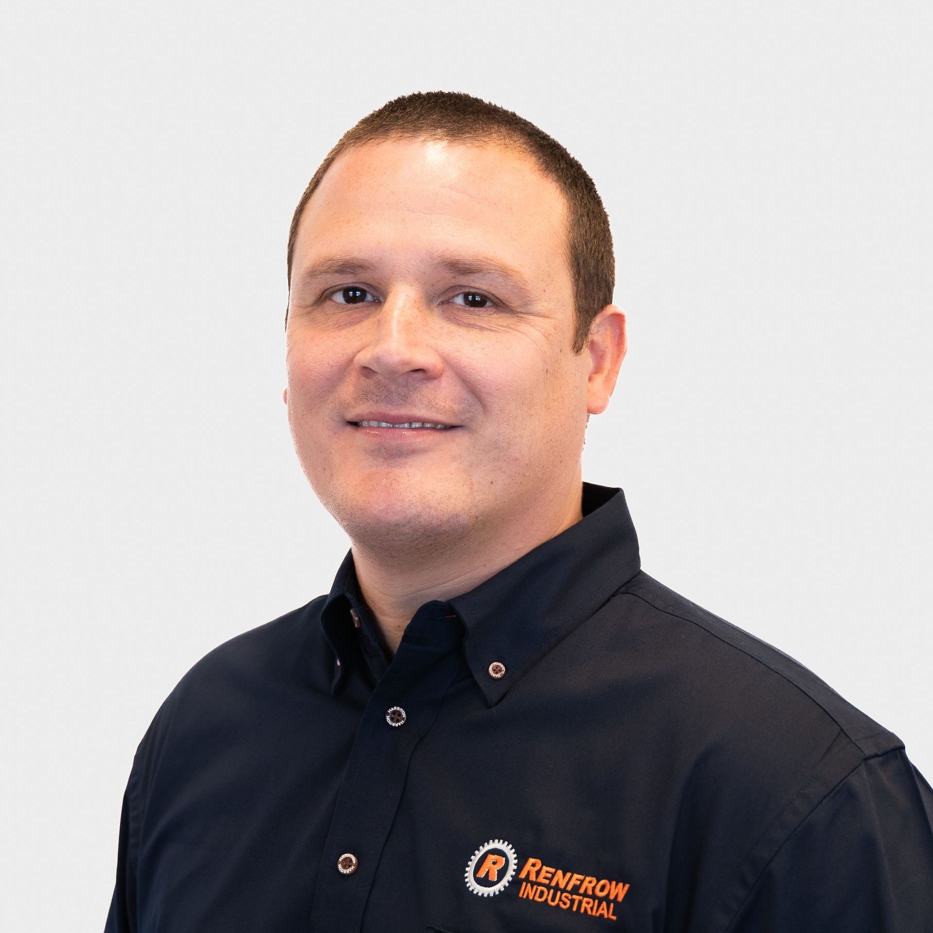 Man in a dark blue shirt with Renfrew Industrial logo, smiling, against a white background.