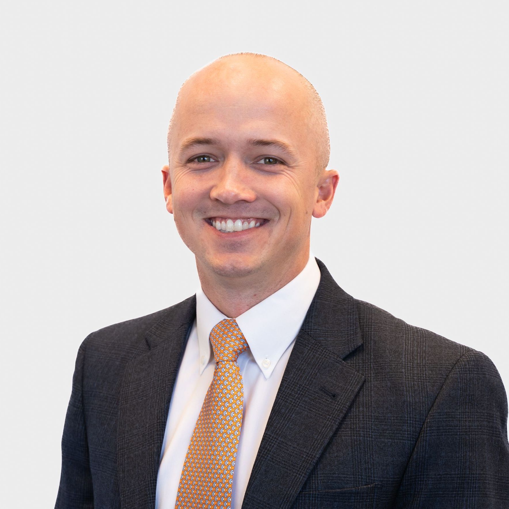 Smiling bald man wearing a suit and tie, posing against a light gray background.