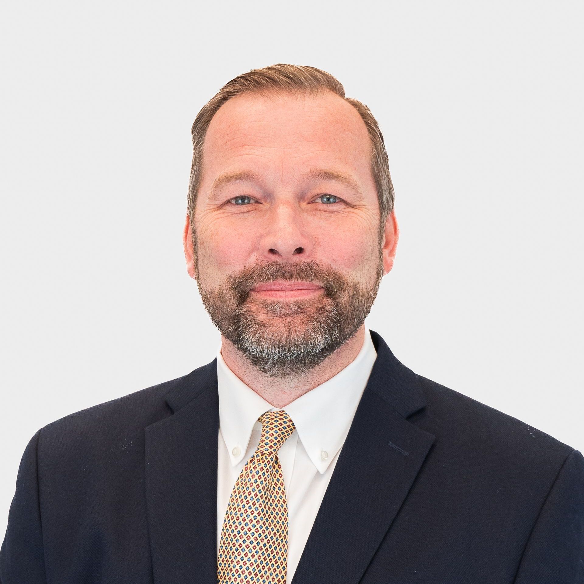 Man in a suit and tie, smiling, against a white background.