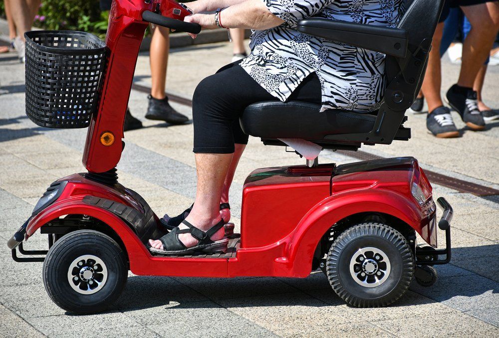 A Woman Is Riding a Red Mobility Scooter on A Sidewalk — Toukley World of Bikes In Toukley, NSW