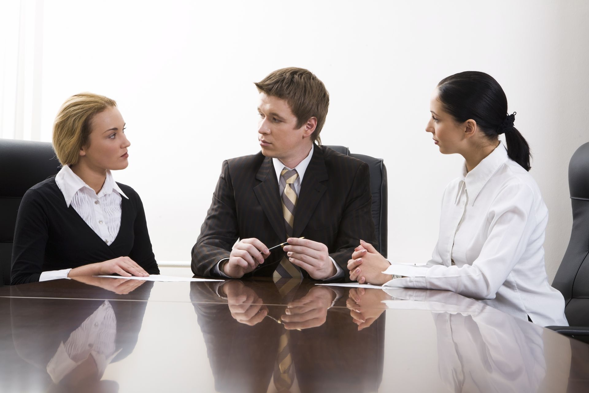 Three people in business attire at a conference table, conversing.