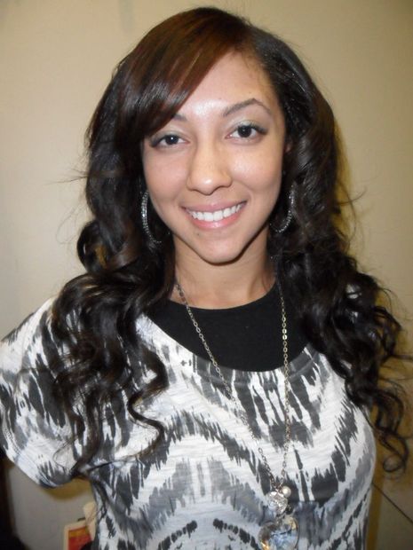 A woman with long hair and a necklace smiles for the camera.