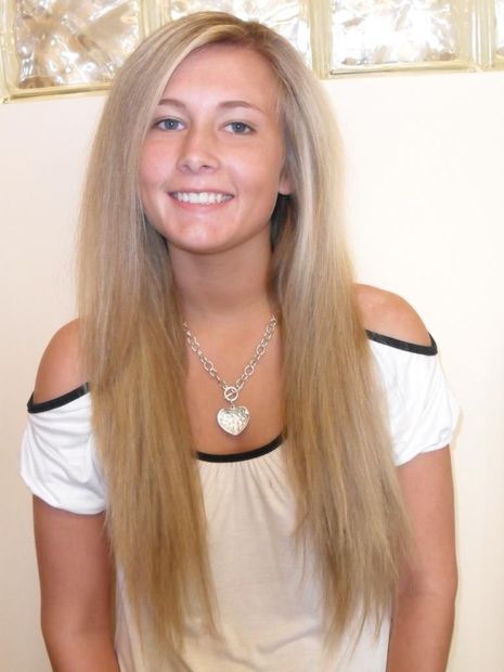 A woman with long blonde hair is wearing a necklace and smiling.