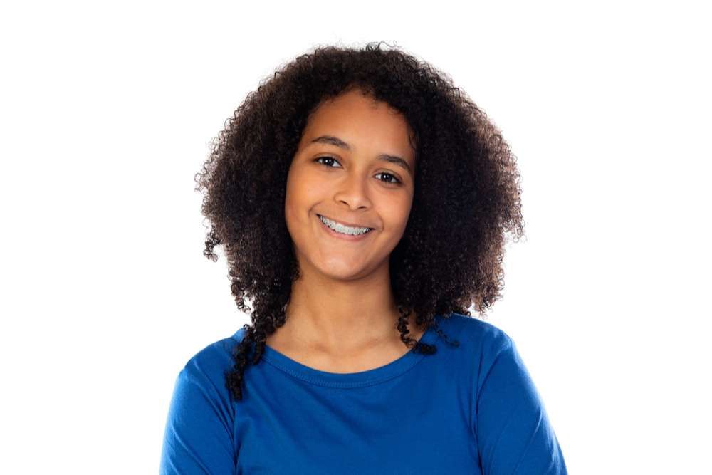 A young girl with braces on her teeth is wearing a blue shirt and smiling.