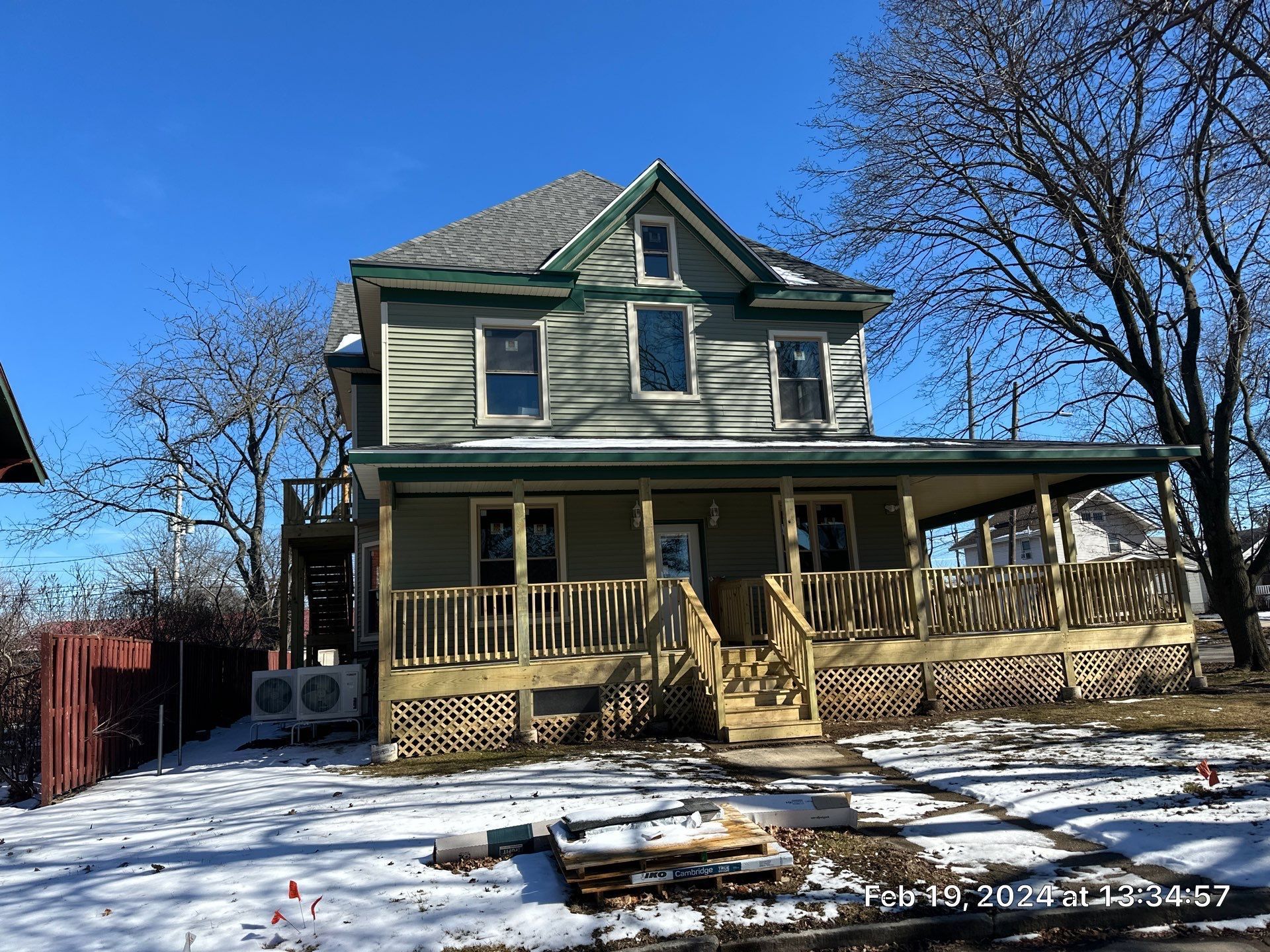 Two-story house with a front porch and snow-covered yard under a clear blue sky